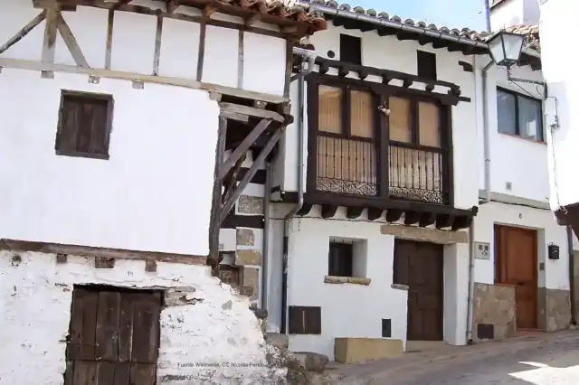 Calle con pendiente de Guisando que muestra viviendas de arquitectura popular con entramados de madera en blanco y pardo.